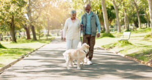 senior couple walking their dog outside on a paved trail